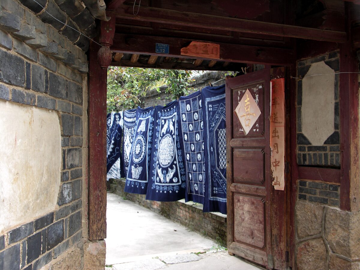 Indigo-dyed cloths hanging in a doorway of a stone-walled lane in Baisha
