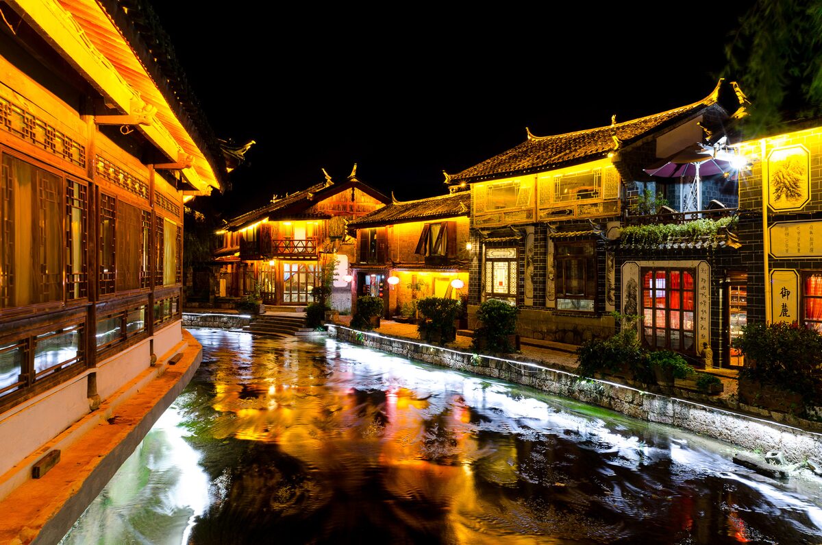Lit wooden houses reflected in a Lijiang Old Town canal at night