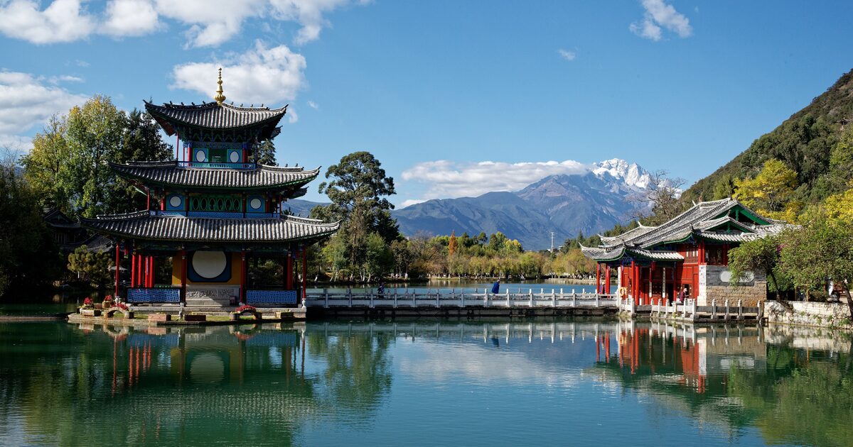 The Black Dragon Pool in Lijiang, a red-pillared pagoda and pavilion mirrored in the water with the snow peaks of Jade Dragon Snow Mountain behind