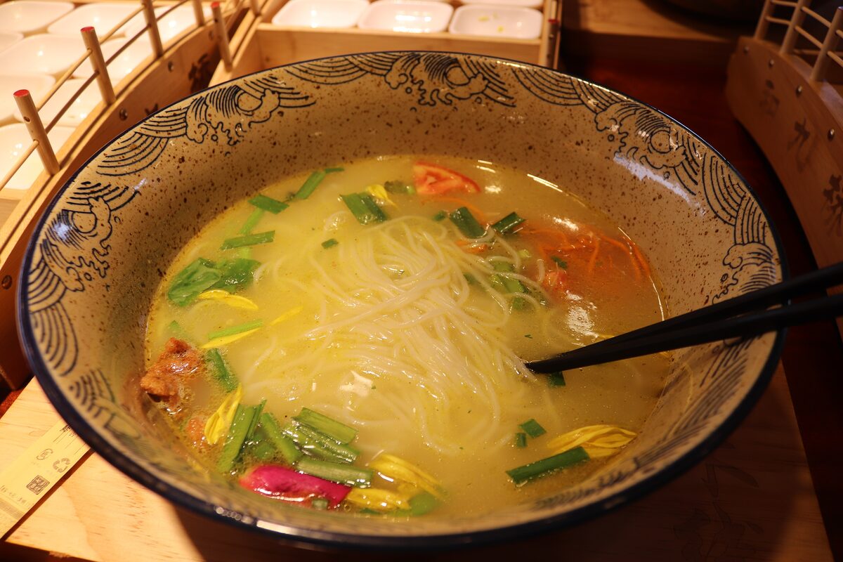 A bowl of crossing-the-bridge rice noodles in clear broth with spring onion and herbs