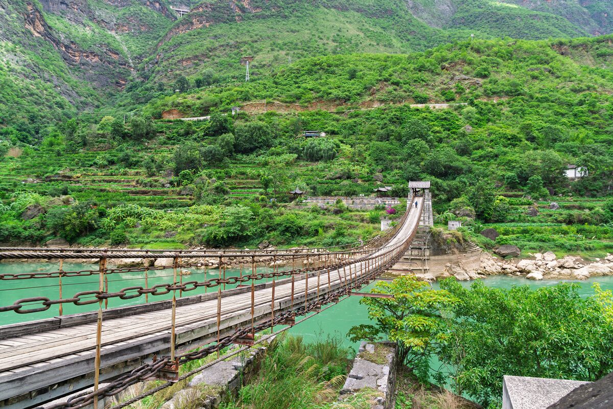 An iron-chain suspension bridge over the green Jinsha River, with terraced hillsides behind