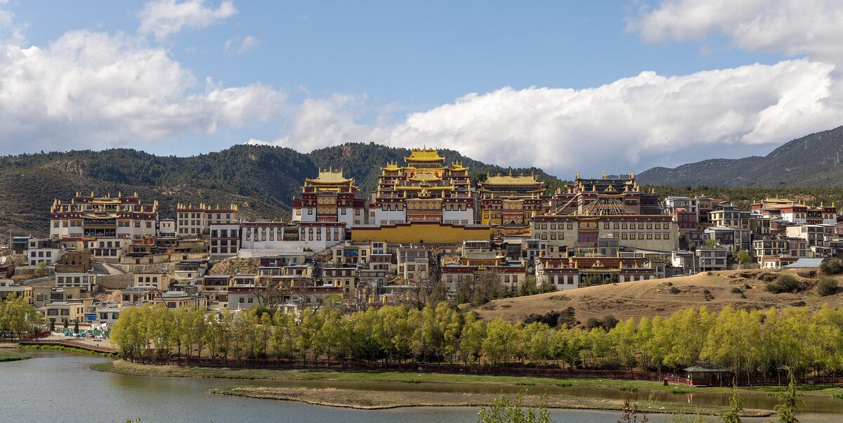 Songzanlin Monastery rising up a hillside above a lake, its golden roofs under a blue sky