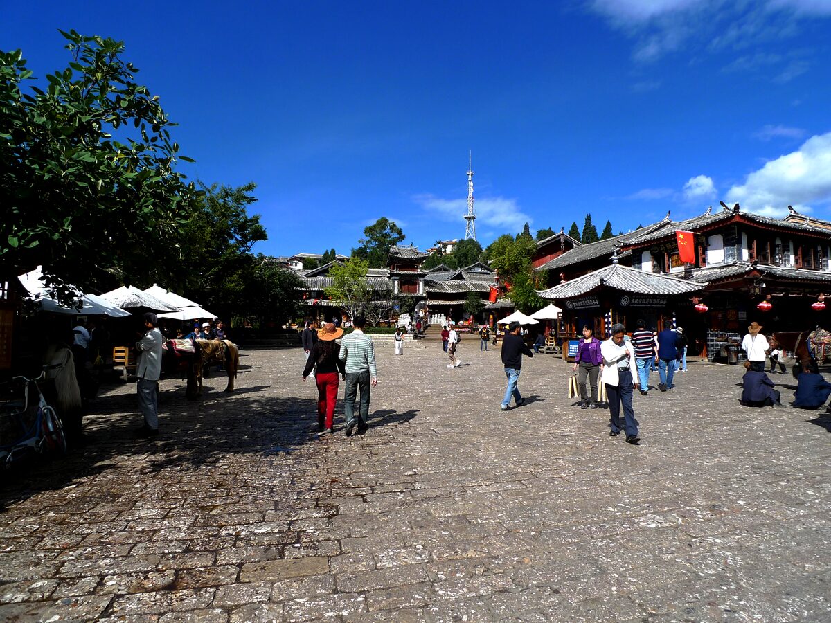 Sifang Street, the cobbled market square of Lijiang Old Town, with a few strollers and tiled-roof houses under a blue sky