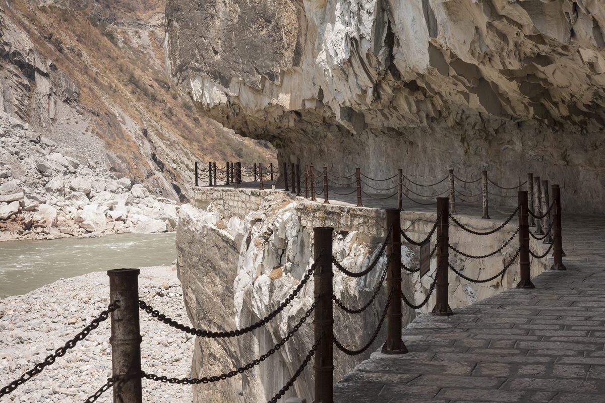 A paved path with chain railings cut into the cliff above the Jinsha River in Tiger Leaping Gorge