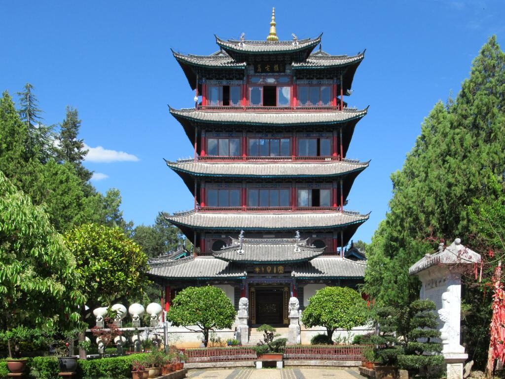 The five-tier Wangu Tower with red-framed windows and tiered tiled roofs, seen across a garden court under a blue sky