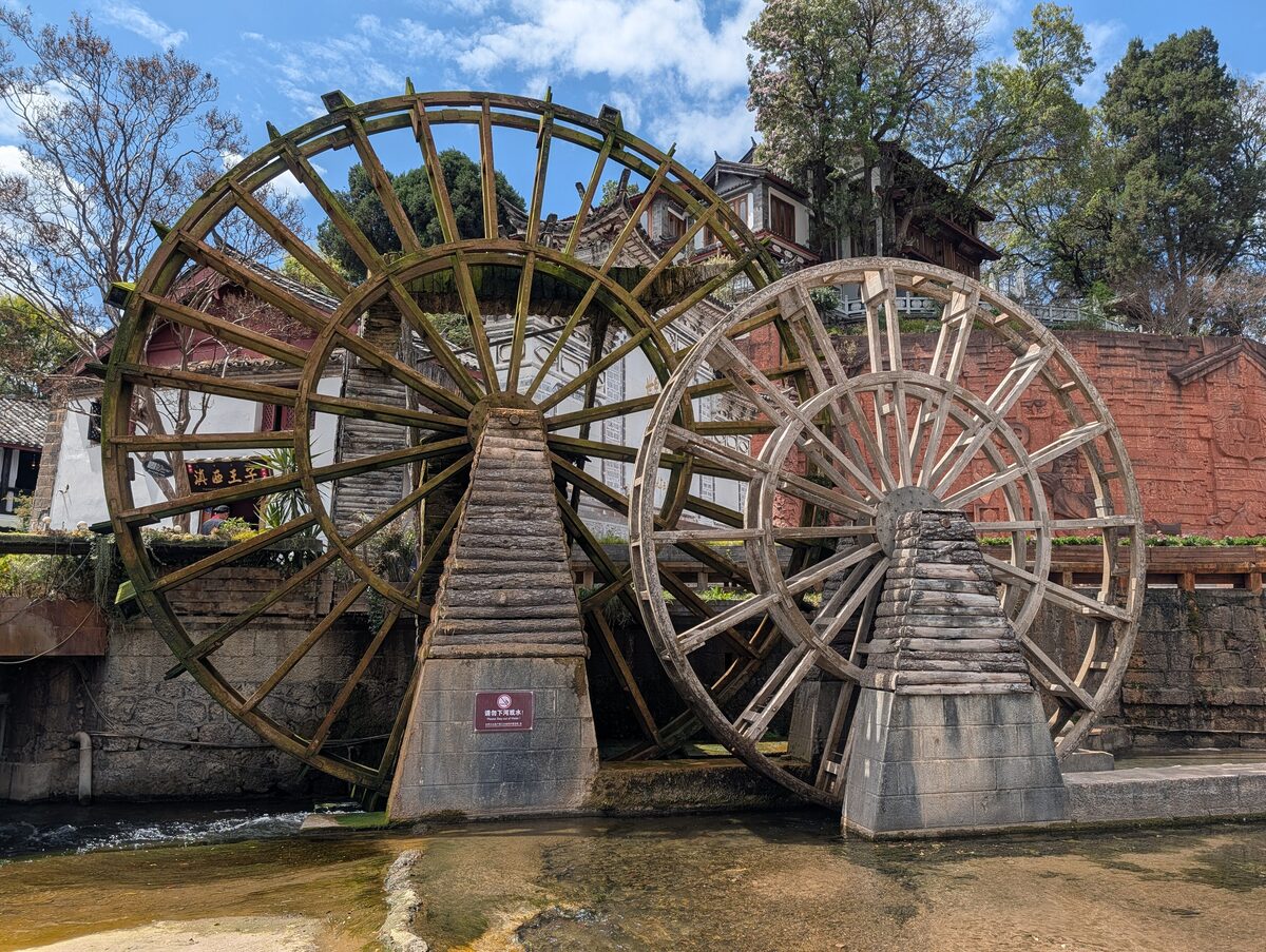 The two big wooden waterwheels at the entrance to Lijiang Old Town, with a red earth wall and old houses behind