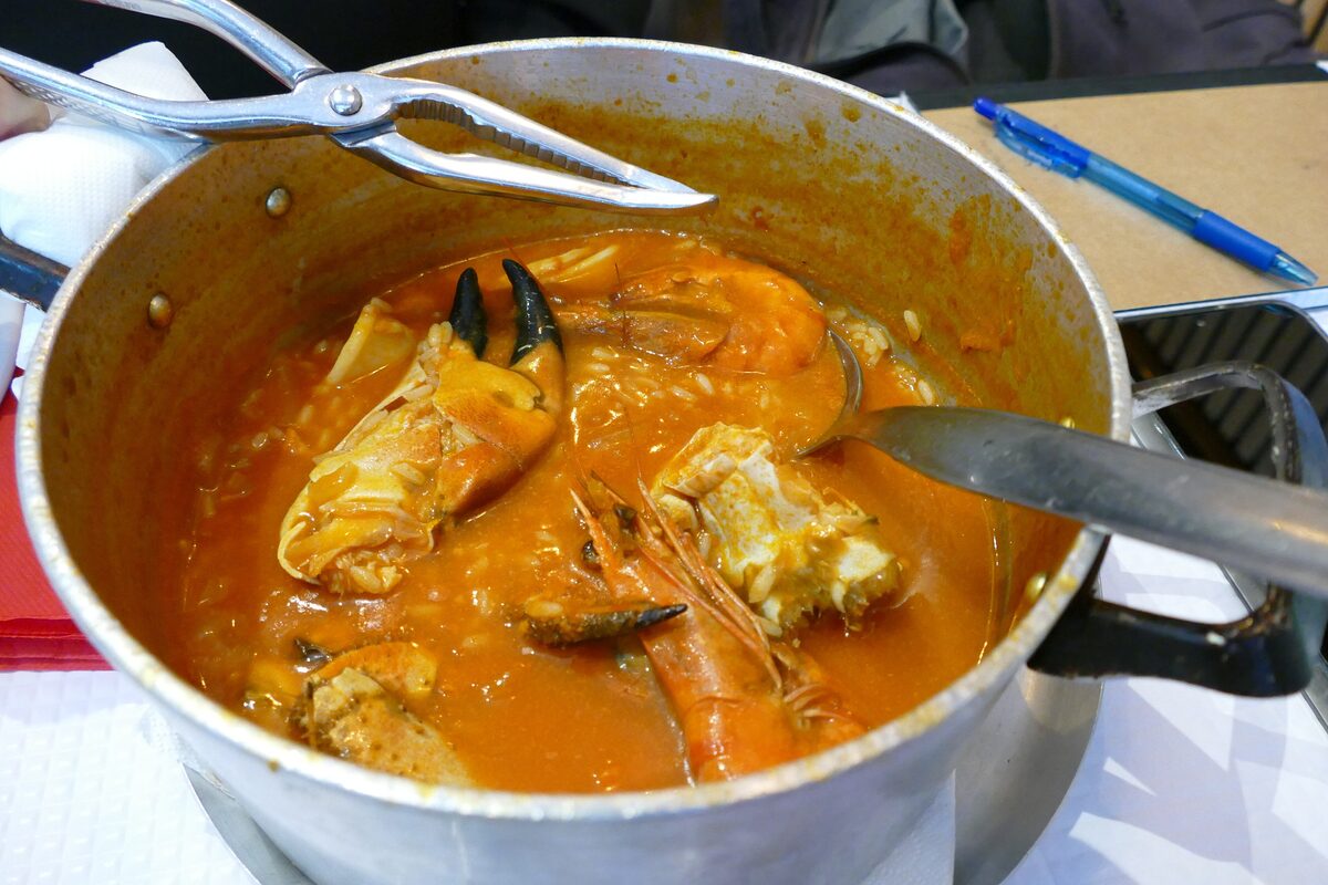 A pot of seafood rice stew with prawns and crab in an orange broth