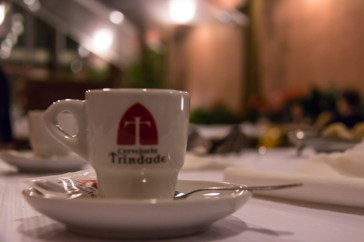 A small white espresso cup with the Cervejaria Trindade logo on a saucer