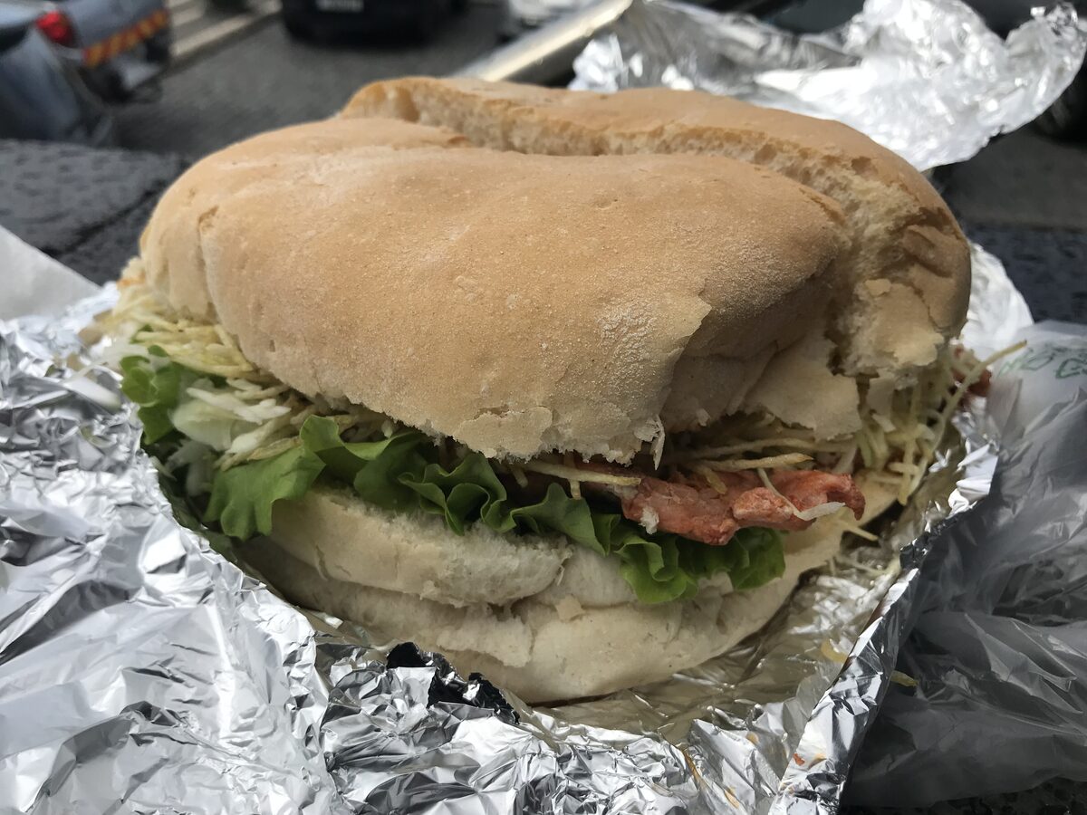 A bifana, a pork sandwich with lettuce, in a crusty roll on foil