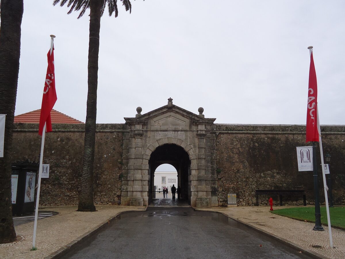 The gate of the Cascais Citadel, with two red flags and palm trees in front