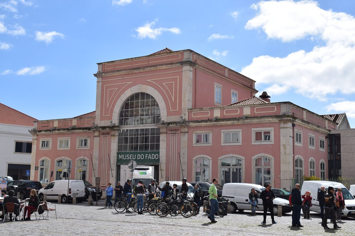 The pink facade of the Museu do Fado on Largo do Chafariz de Dentro, with its arched window and green sign, under a blue sky