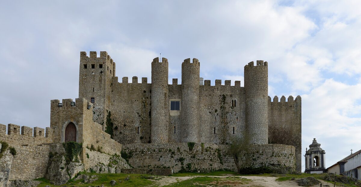 The crenellated towers of Óbidos castle on its hill under a bright cloudy sky