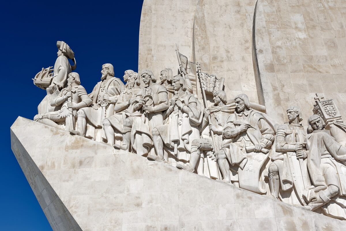 Explorers carved along the prow of the Monument to the Discoveries in Belém, led by Henry the Navigator, against a deep blue sky