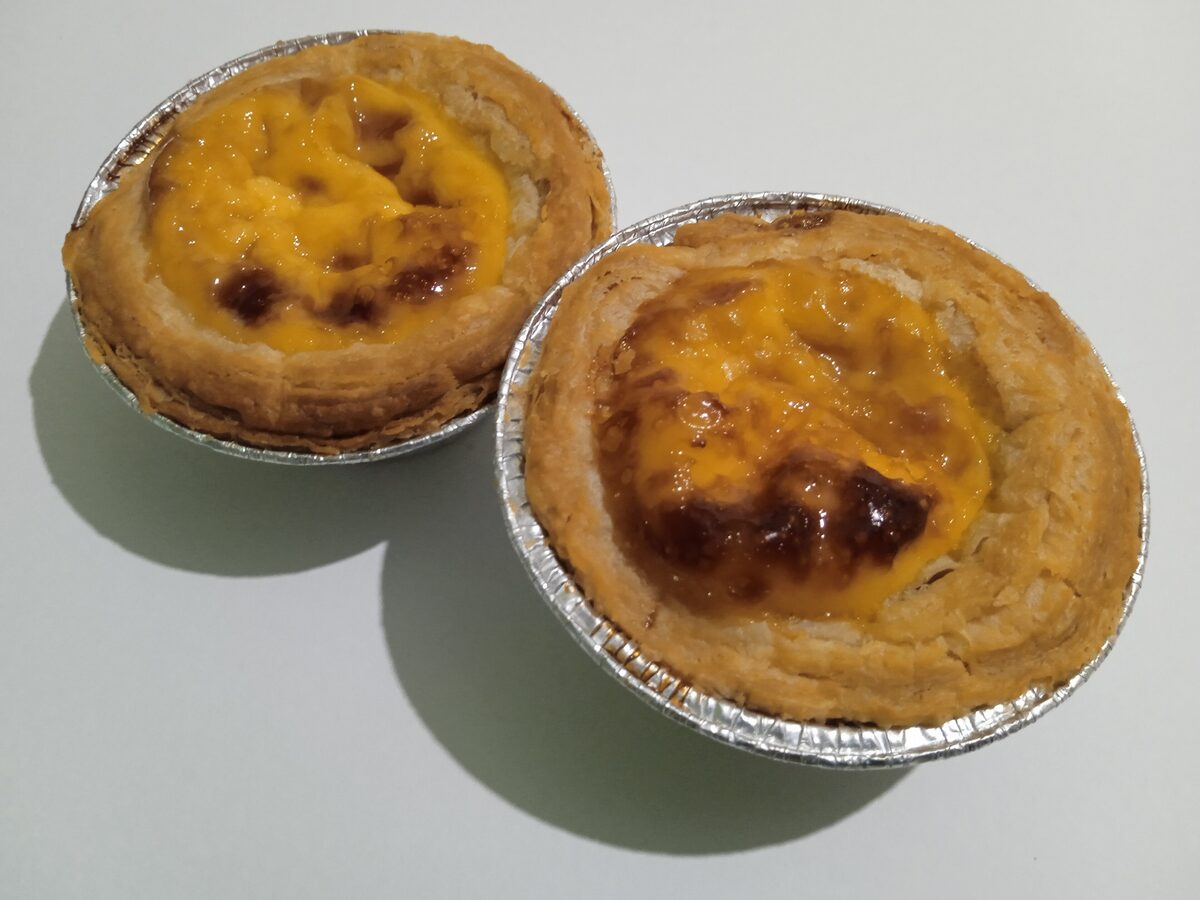 Two pastéis de nata in foil cases, with blistered golden tops