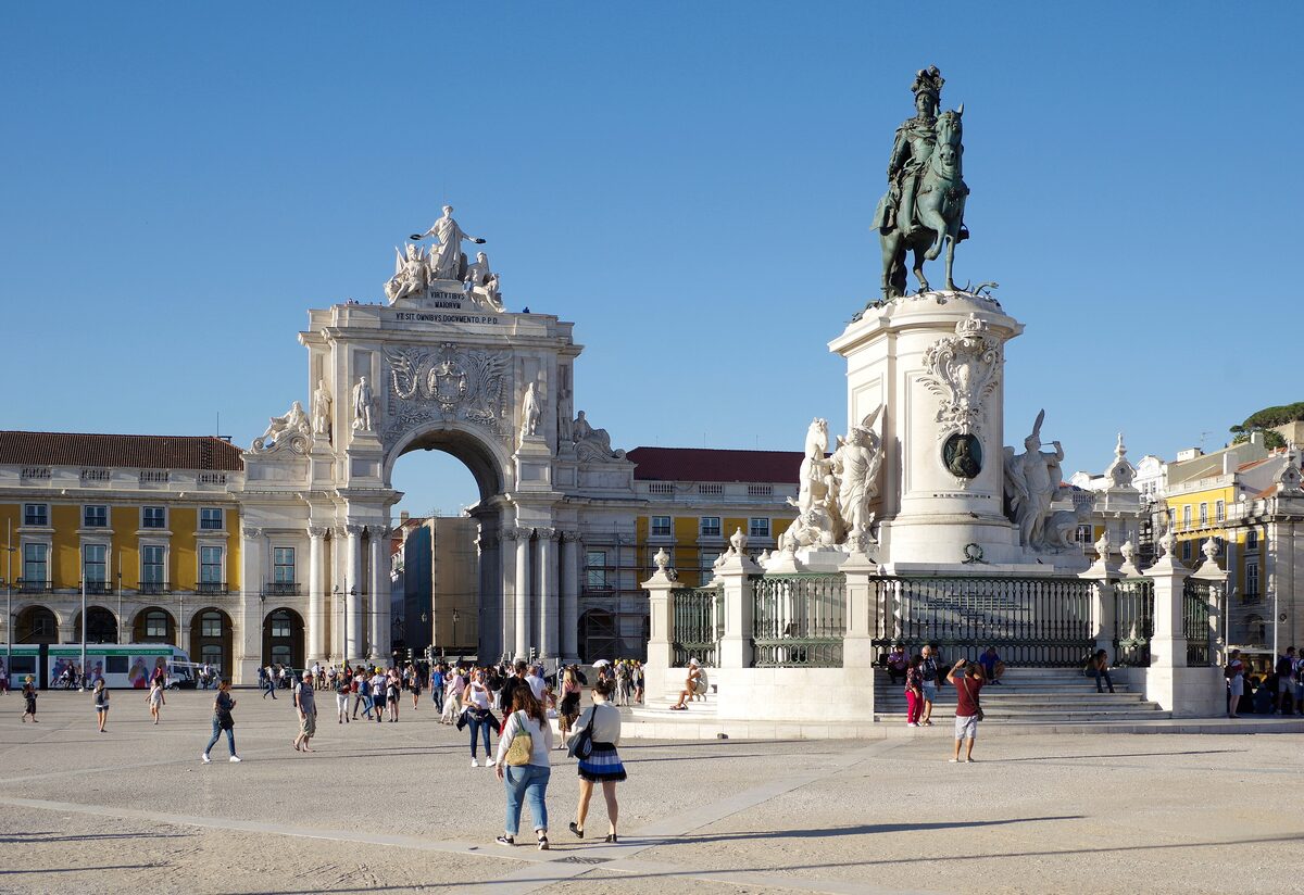 The Rua Augusta Arch and the bronze statue of King José I on Praça do Comércio, under a clear blue sky