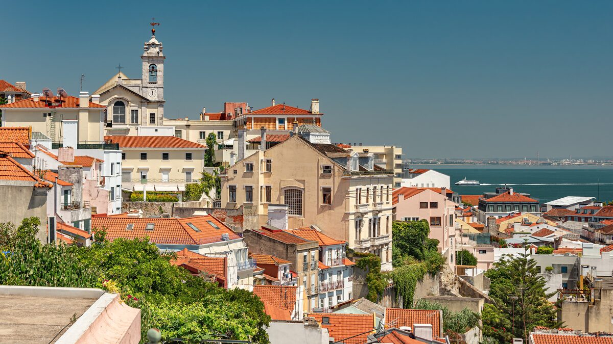 Terracotta roofs and a church tower tumbling down toward the Tagus, seen from Miradouro de Santa Catarina