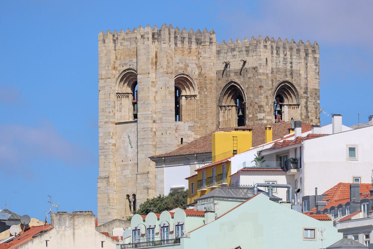 The fortress-like twin towers of the Sé cathedral rising above Alfama rooftops under a blue sky