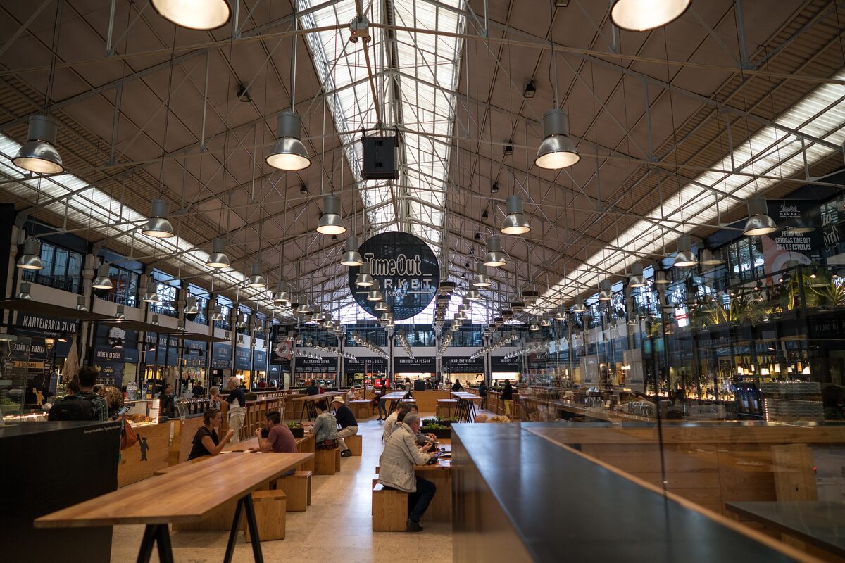 The iron-framed hall of Time Out Market with long wooden tables and the market sign hanging from the roof