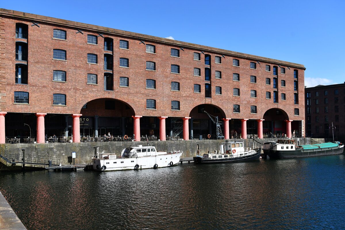 The red-brick warehouses and iron columns of the Royal Albert Dock in Liverpool, reflected in the still water of the dock