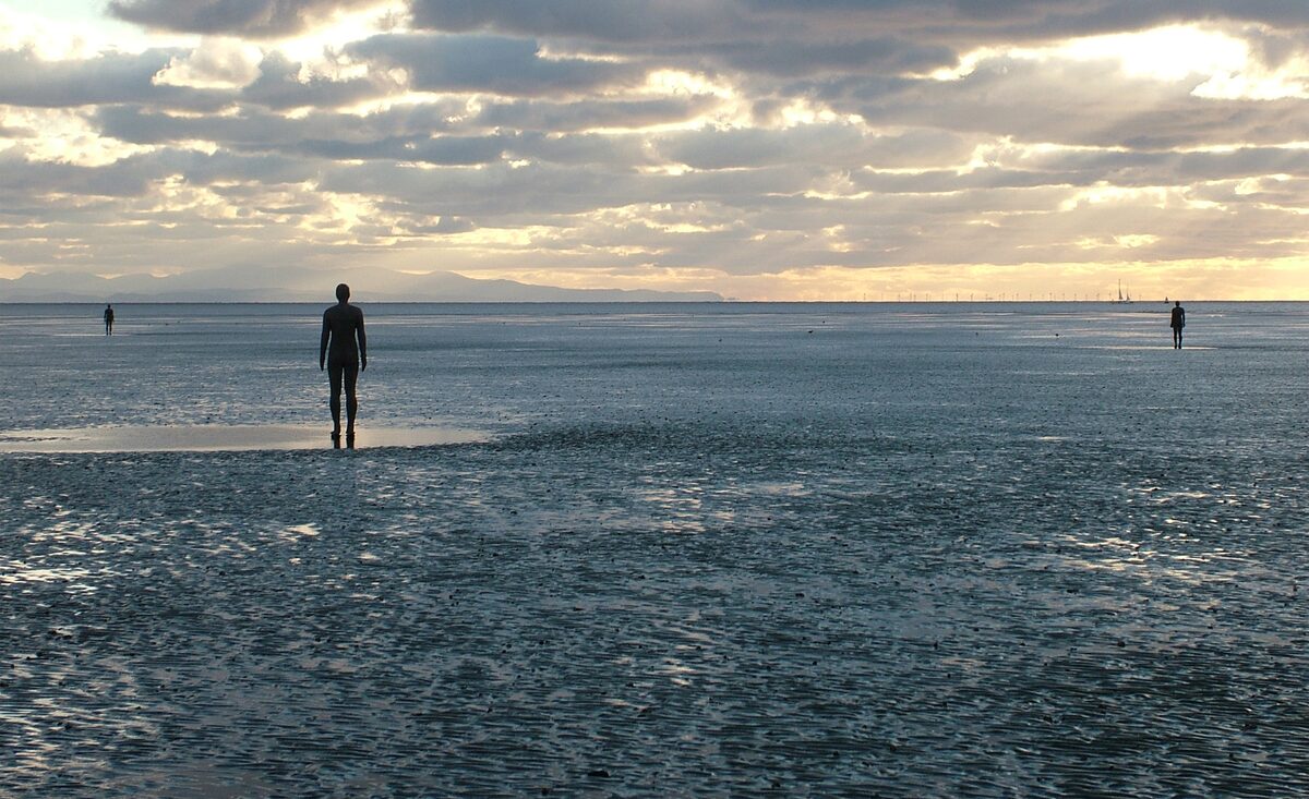 One of Antony Gormley's iron figures standing on Crosby Beach, looking out to sea at sunset