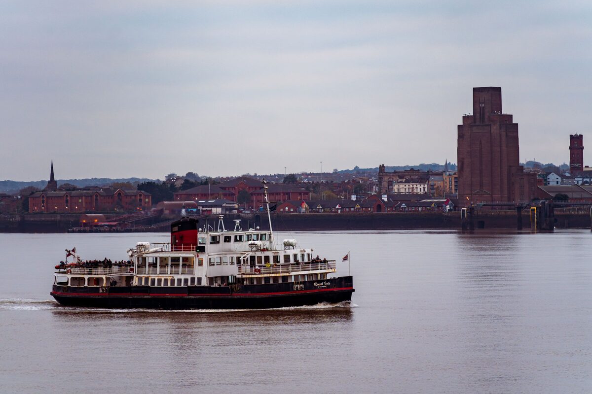 A Mersey ferry crossing the river, with the Wirral shore and the Birkenhead tunnel tower behind