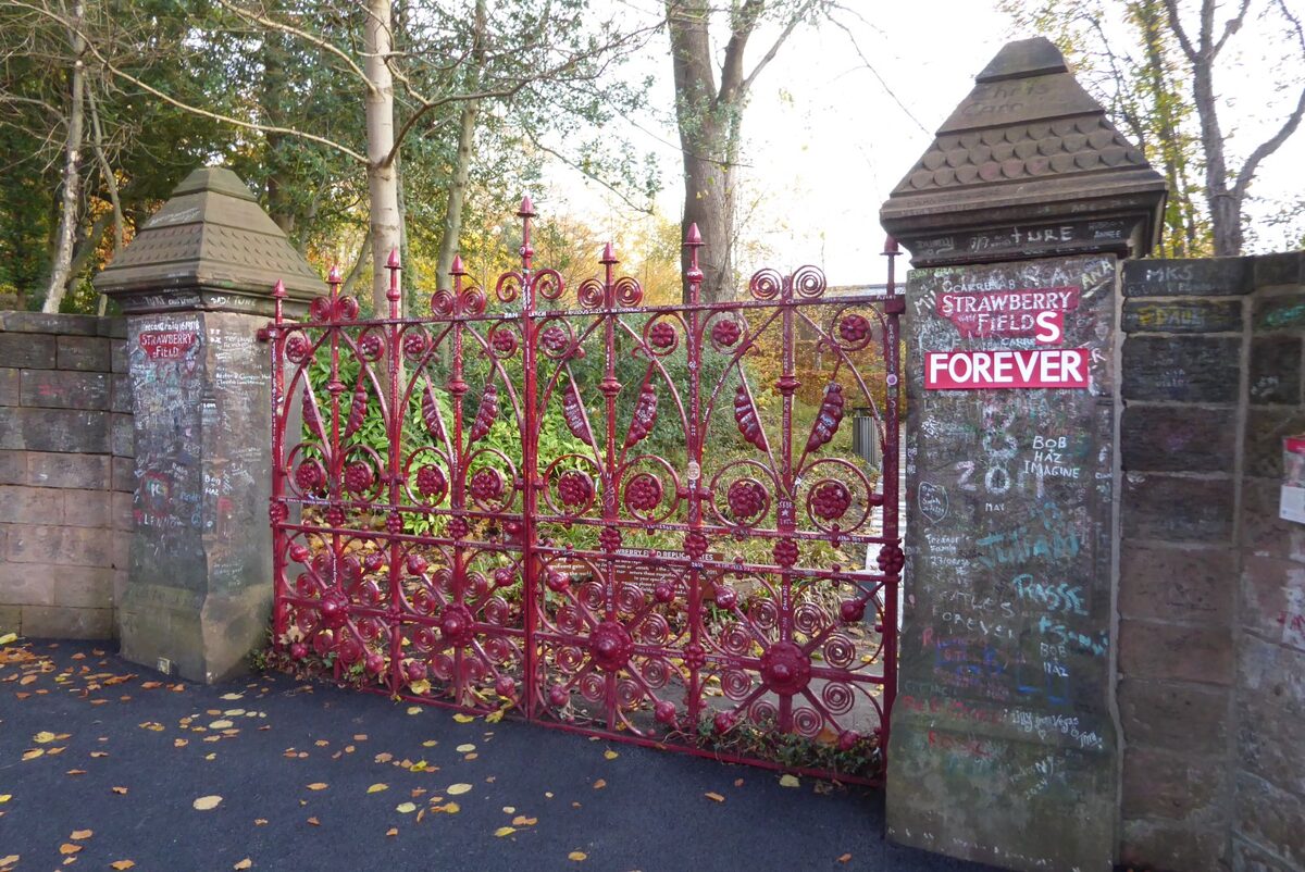 The red iron gates of Strawberry Field in Liverpool, with a stone gatepost and trees behind