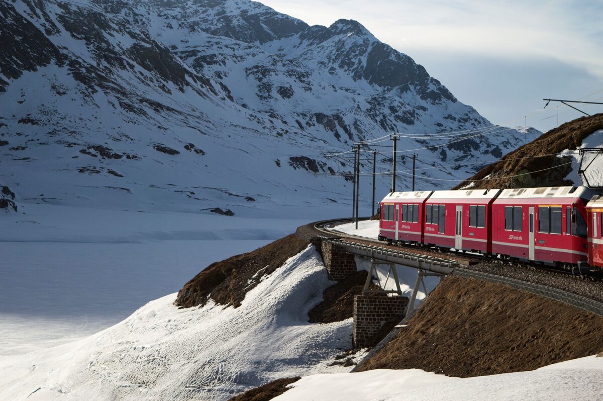 A red Bernina Express train on a snowy bridge above a frozen lake in the Swiss Alps