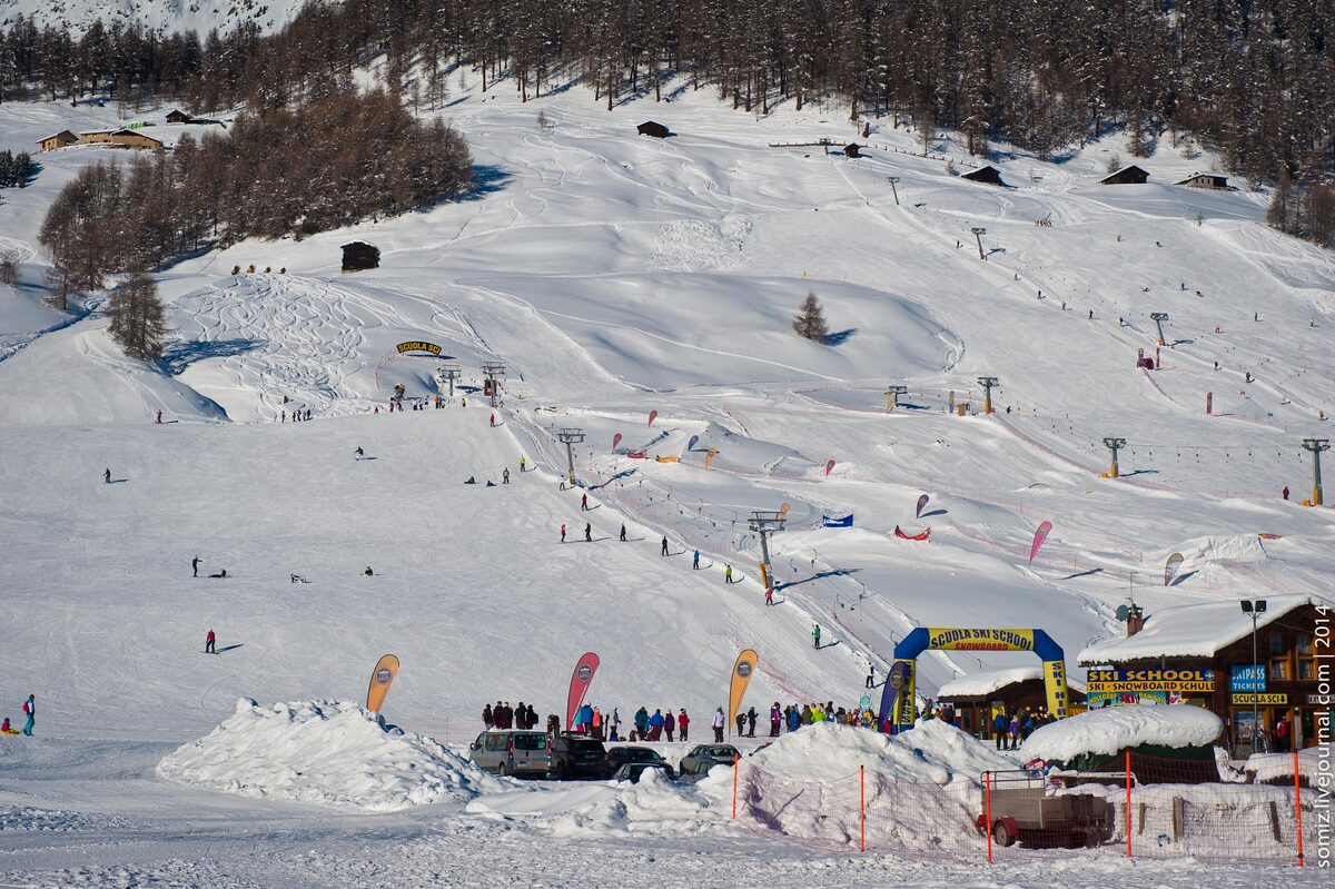 A beginner slope in the snow with a tow lift, colored flags and a ski school hut