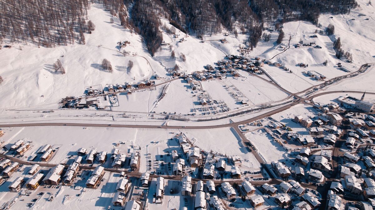 Aerial view of the snow-covered village of Livigno, with chalets and roads on the valley floor and forested slopes above