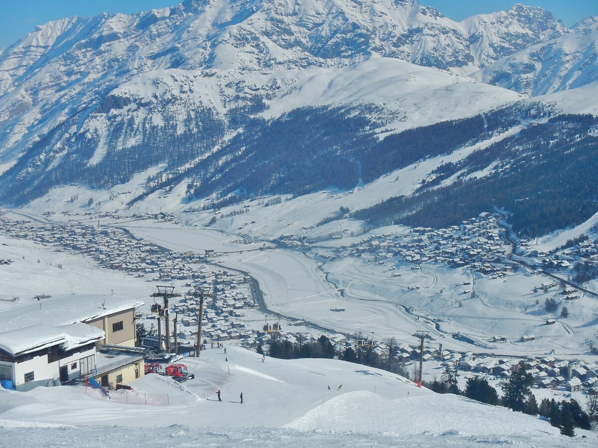 Looking down from the Carosello 3000 slopes over the snowy valley and the village of Livigno, with a lift station in the foreground