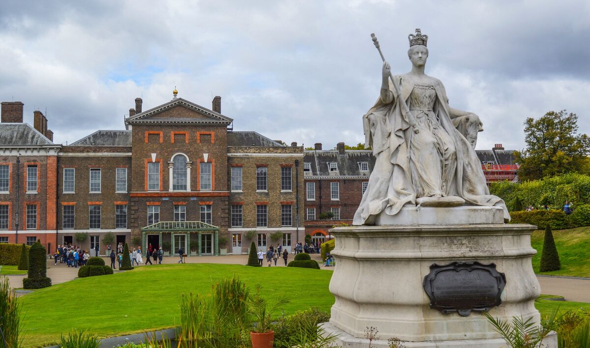 The red-brick Kensington Palace with a statue of Queen Victoria in front, in Kensington Gardens