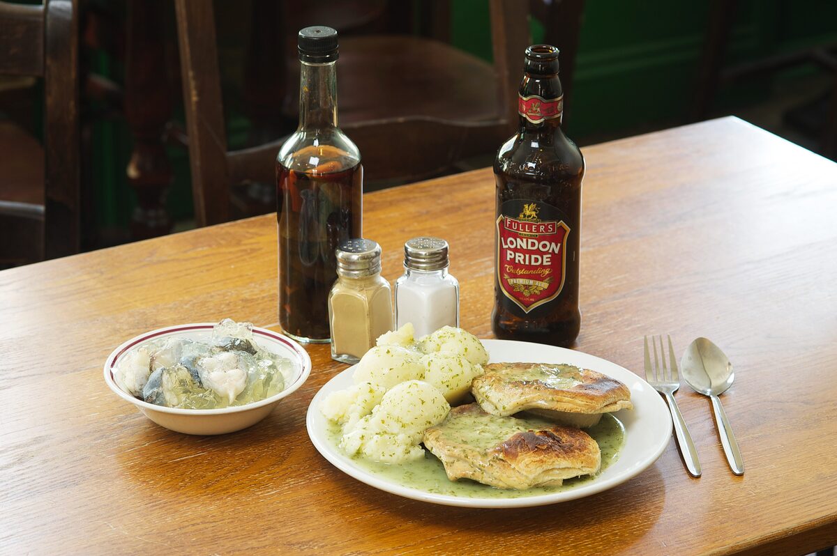 Pie and mash with green parsley liquor, a bowl of eels and bottles of vinegar on a pie shop table