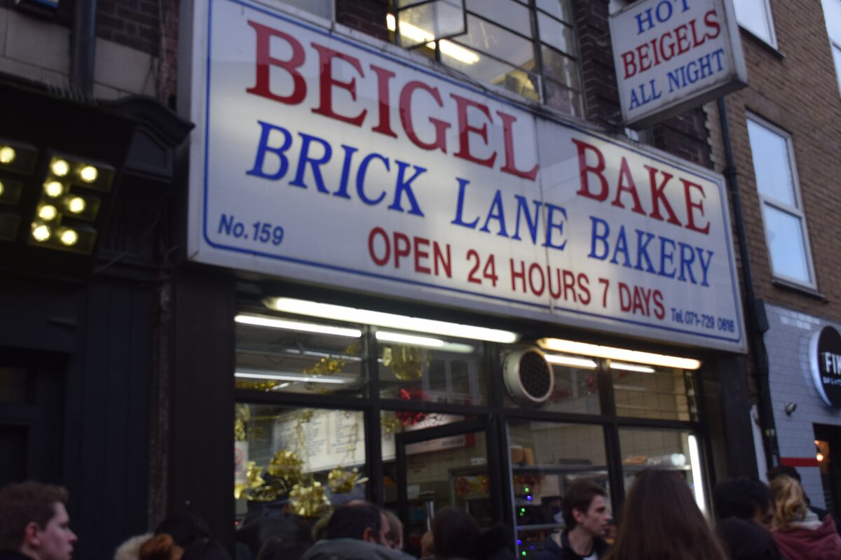 The white sign of Beigel Bake on Brick Lane, open 24 hours, with people queuing inside