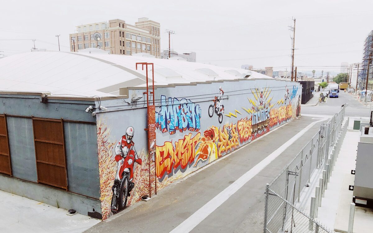 A long street-art mural of riders and bold lettering on a warehouse wall in the Arts District