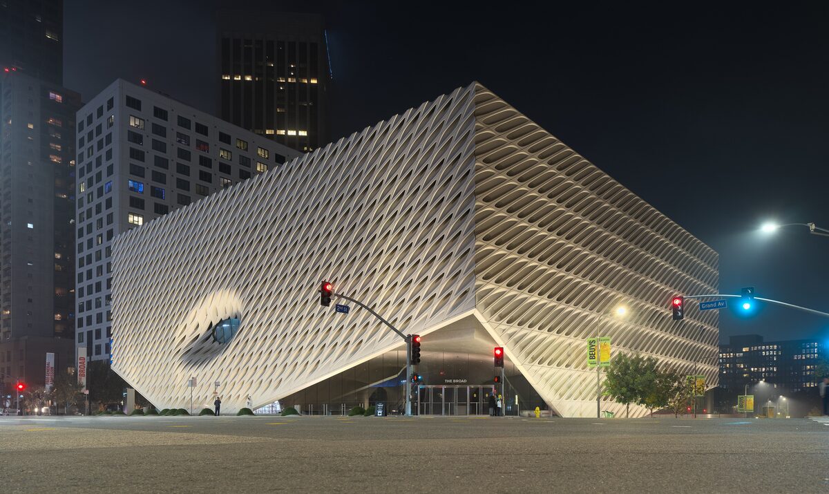 The Broad museum's perforated white veil facade lit at night on Grand Avenue with towers behind it
