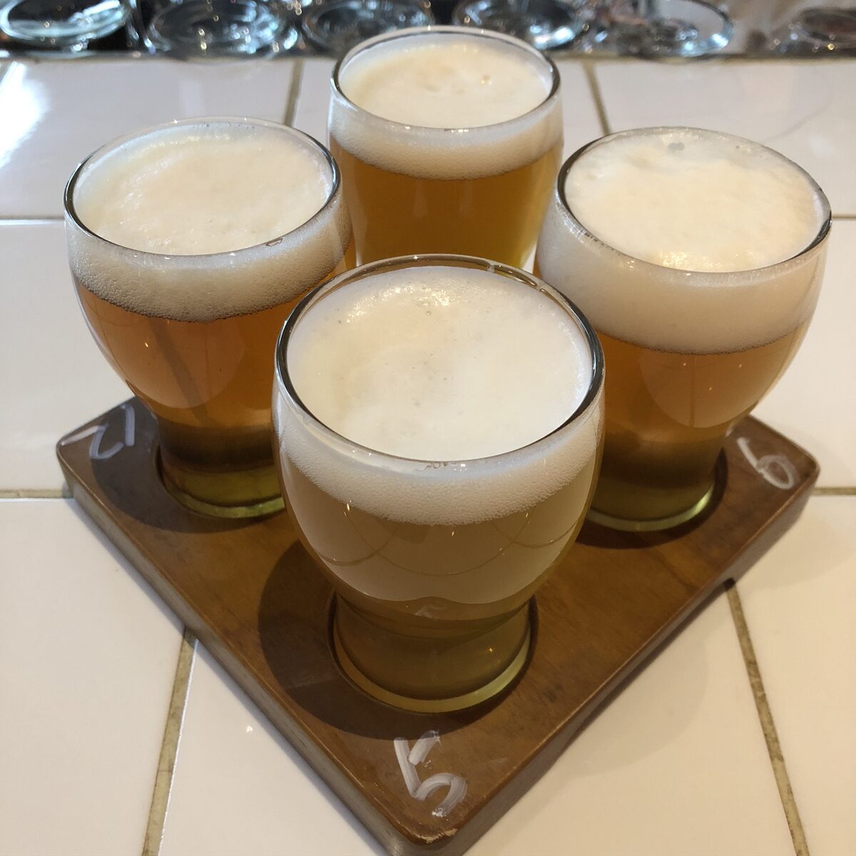 A flight of four small glasses of craft beer with foam on a wooden paddle