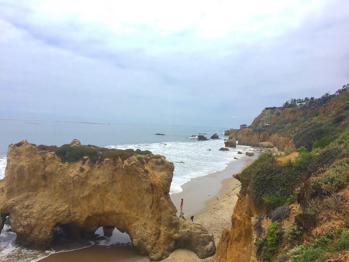 The sea arch and rocky cove at El Matador State Beach, with surf on the sand and cliffs behind