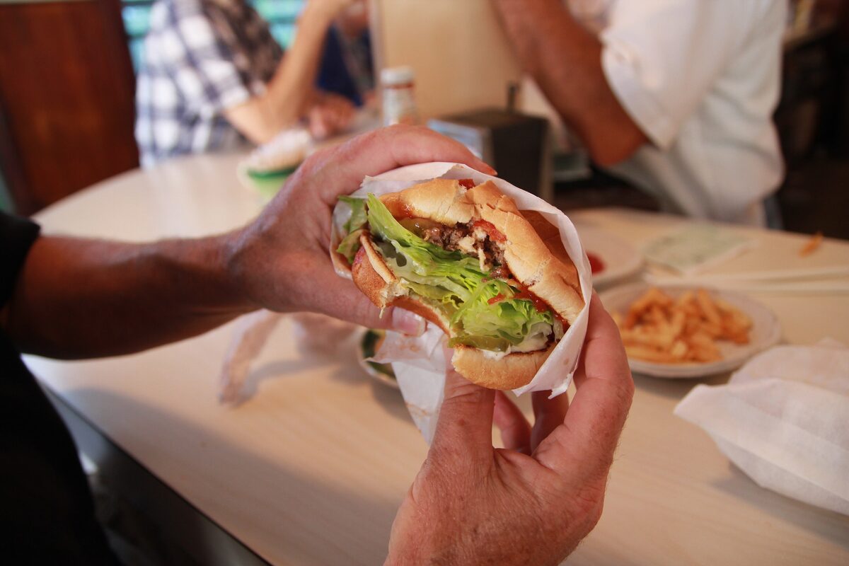 A hand holding a hickory burger wrapped in paper at The Apple Pan counter