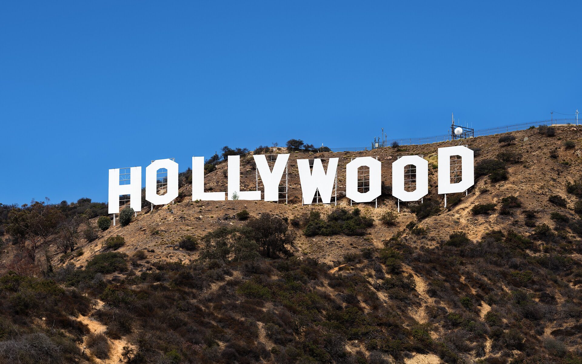 The white Hollywood Sign letters on the dry brown hillside of Mount Lee under a clear blue sky