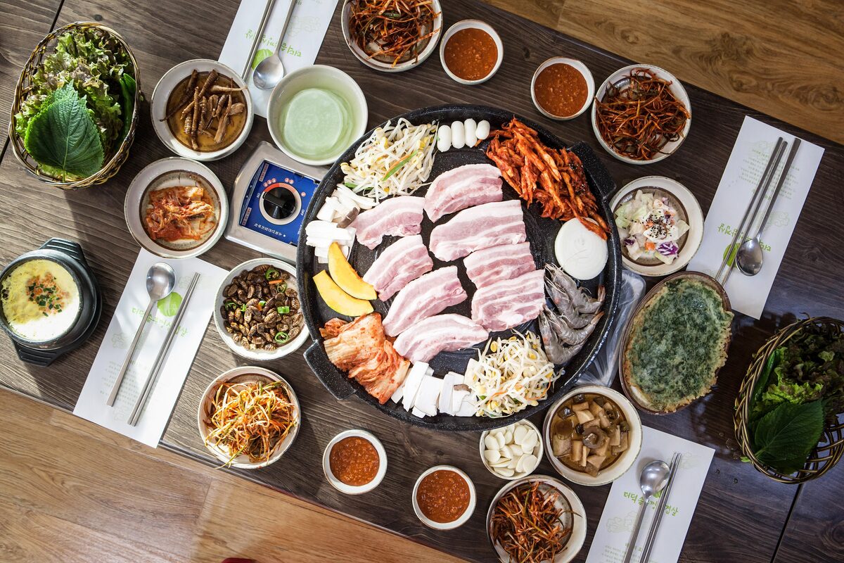 A Korean barbecue table from above, pork belly on the grill surrounded by small side dishes