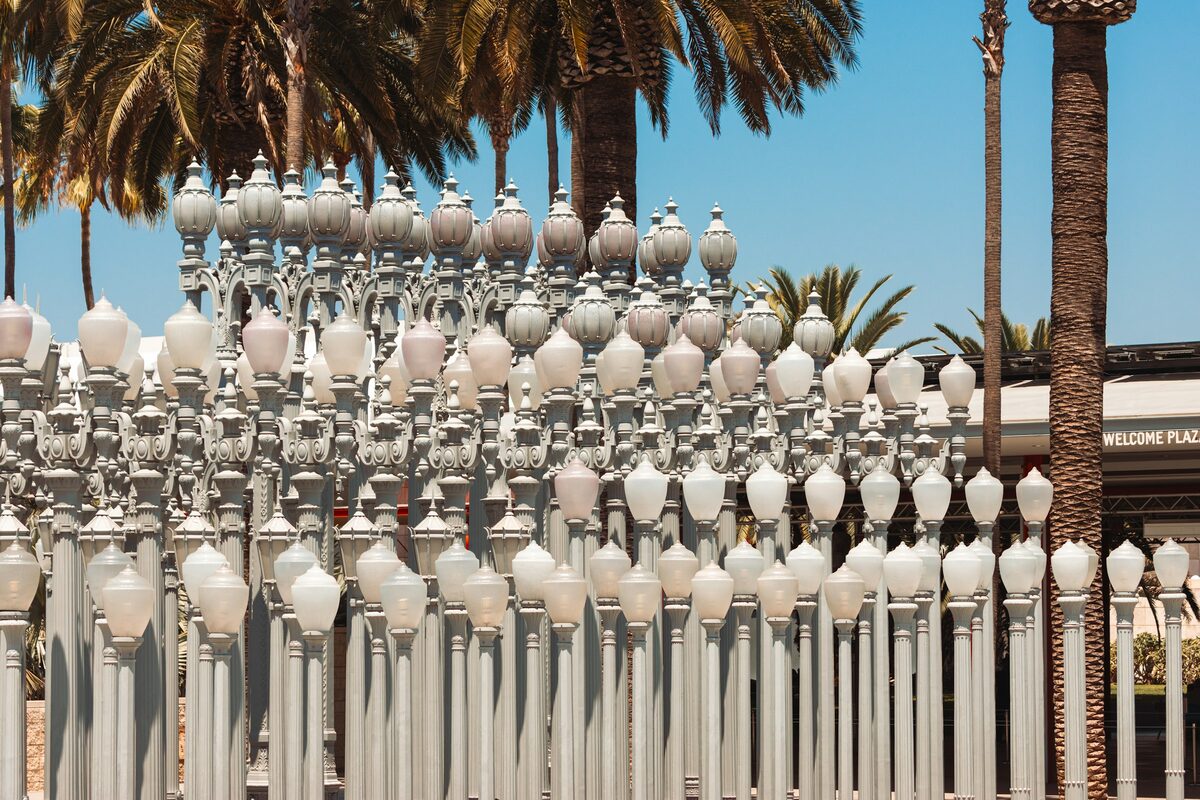 Rows of restored cast-iron street lamps in Urban Light at LACMA under palm trees and a blue sky