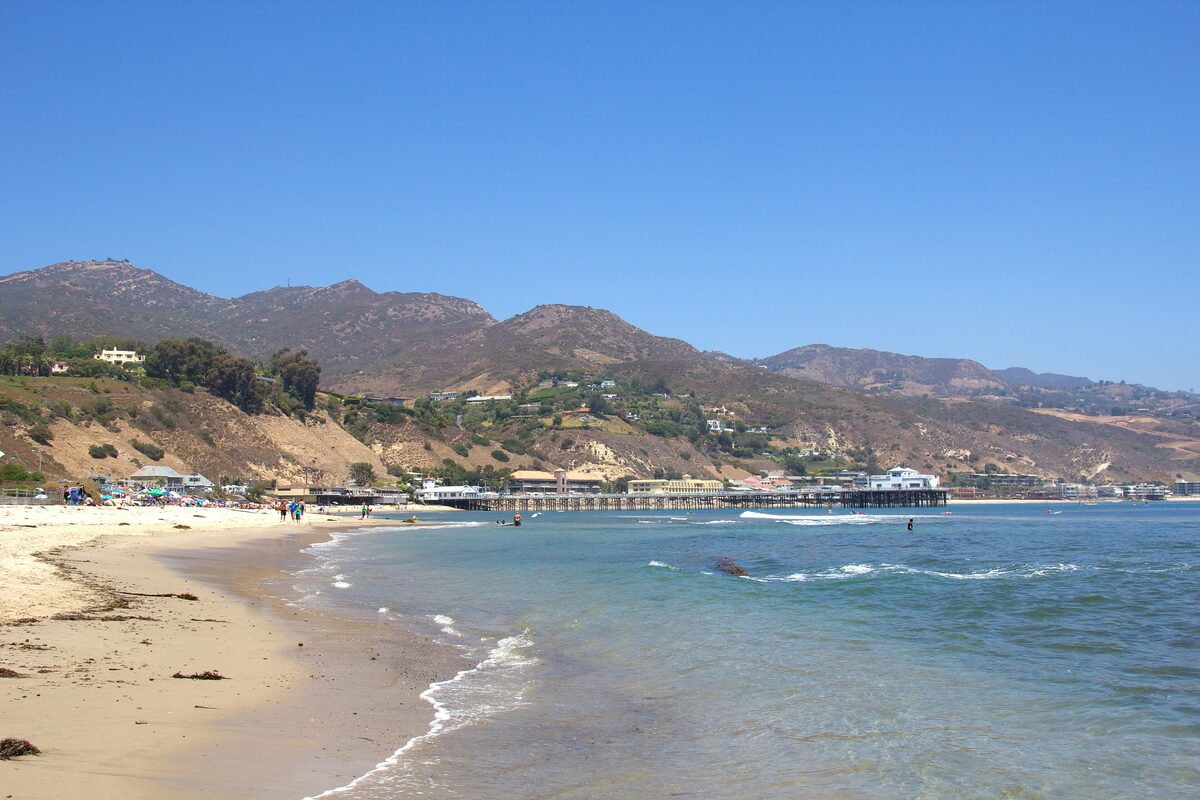 Malibu's sandy beach and blue surf with the pier in the distance below the Santa Monica Mountains