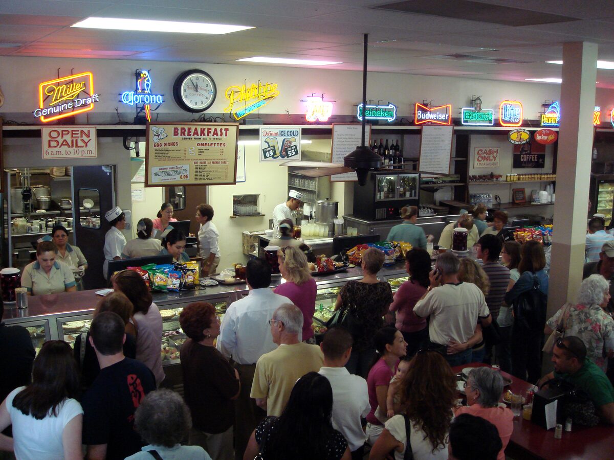 The sandwich counter at Philippe the Original with a crowd waiting under neon beer signs