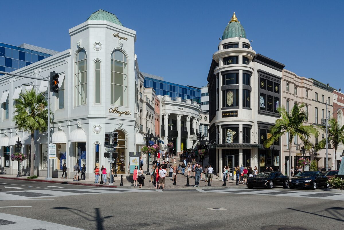 White luxury boutiques and palm trees at a busy corner of Rodeo Drive in Beverly Hills