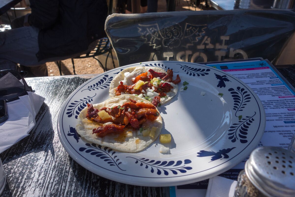 Two al pastor tacos with onion and pineapple on a blue patterned plate