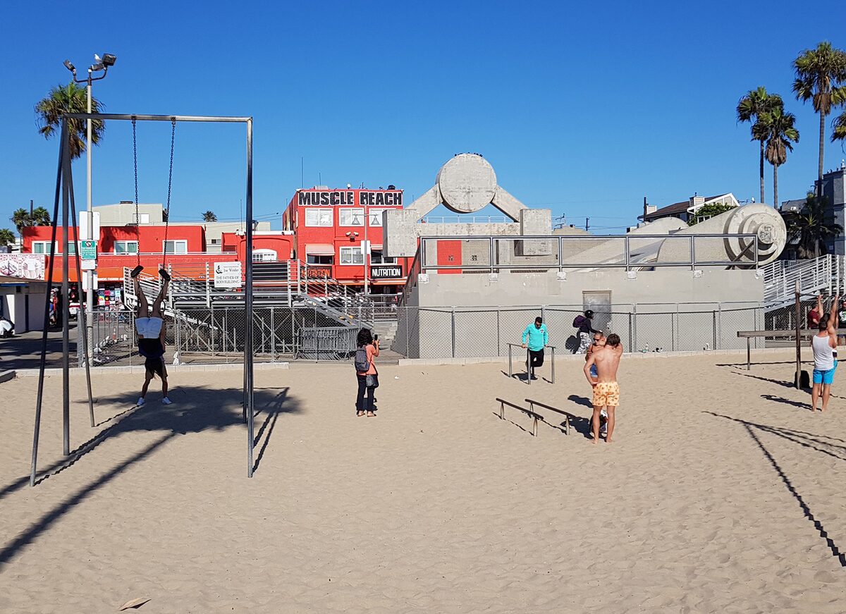 The outdoor gym and red Muscle Beach building on the sand at Venice Beach, with palm trees behind