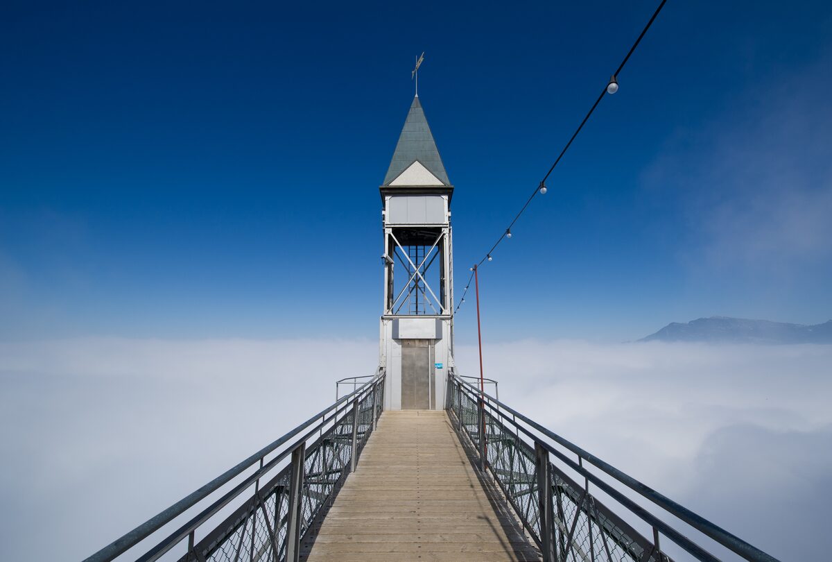 The Hammetschwand Lift tower at the end of its footbridge above a sea of cloud, under a deep blue sky