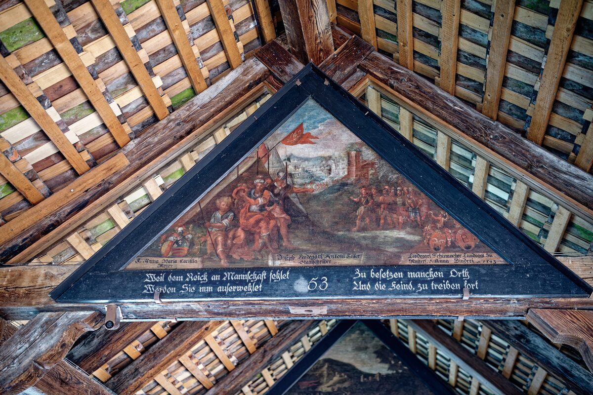 A painted triangular panel under the roof of the Chapel Bridge, framed by the wooden rafters and beams