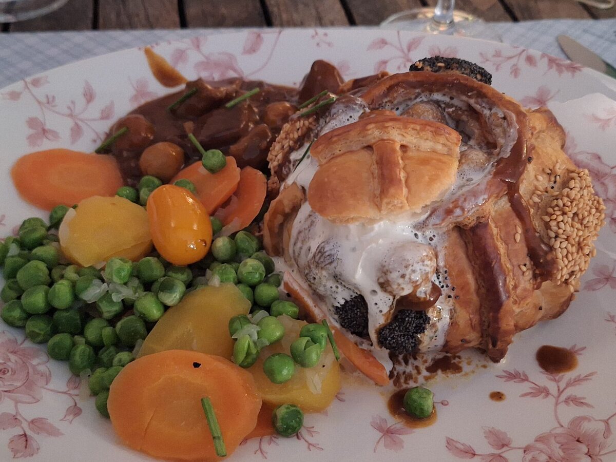 A golden puff pastry case with veal ragout, served with peas and carrots on a plate with a rose pattern