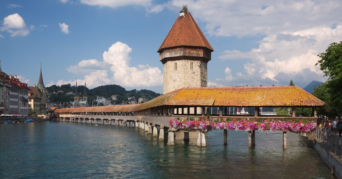 The wooden Chapel Bridge with its stone water tower over the Reuss in Lucerne, flower boxes on the bridge and the old town behind